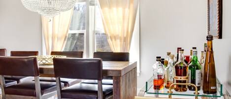 Un comedor con mesa de madera, sillas de cuero, candelabro y vitrina de vidrio con botellas de licor.