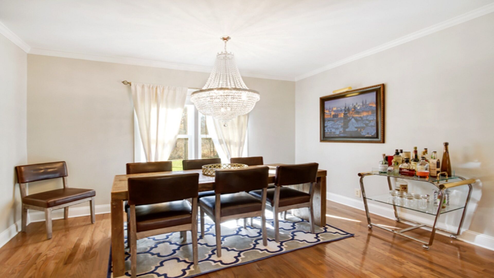 Un comedor con candelabro, mesa de madera, sillas y una vitrina de vidrio con botellas.
