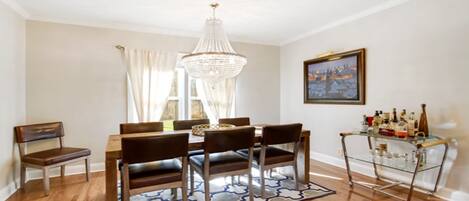 Un comedor con candelabro, mesa de madera, sillas y una vitrina de vidrio con botellas.