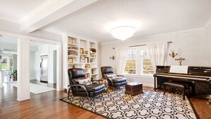 A spacious living room with a grand piano, leather armchairs, and a large bookshelf. - Location!!! Location!!! Berkshire Glamour (and comfort) Meets Town And Country (Stockbridge)
