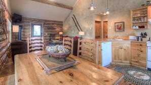 Ein rustikales Blockhaus-Interieur mit einem Holzesstisch, Kamin, einer Küche mit Holzausstattung und einem Deckenventilator.