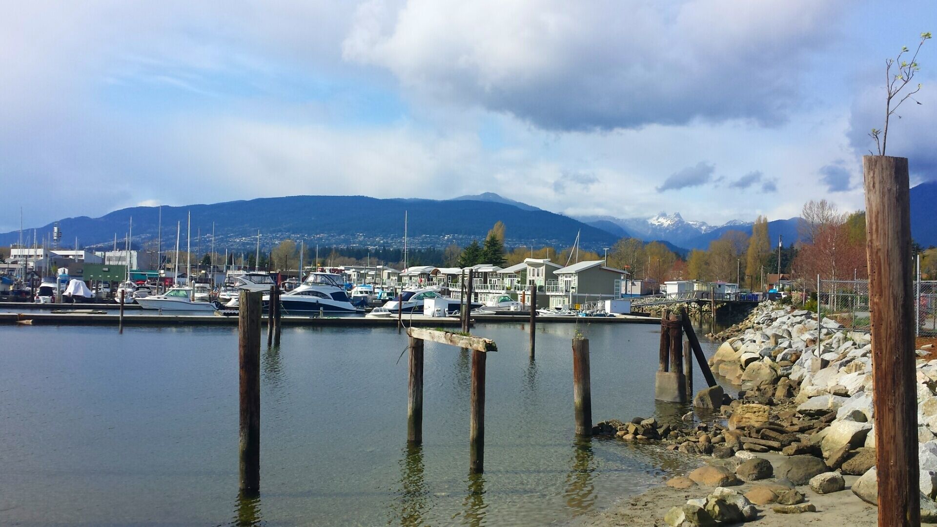 Un port de plaisance avec des bateaux amarrés, une côte rocheuse et des montagnes en arrière-plan.