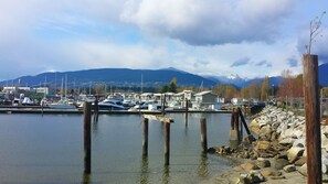 A marina with boats docked, a rocky shoreline, and mountains in the background.