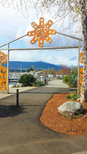 A metal archway with a sun design, leading to a paved path with rocks and shrubs.