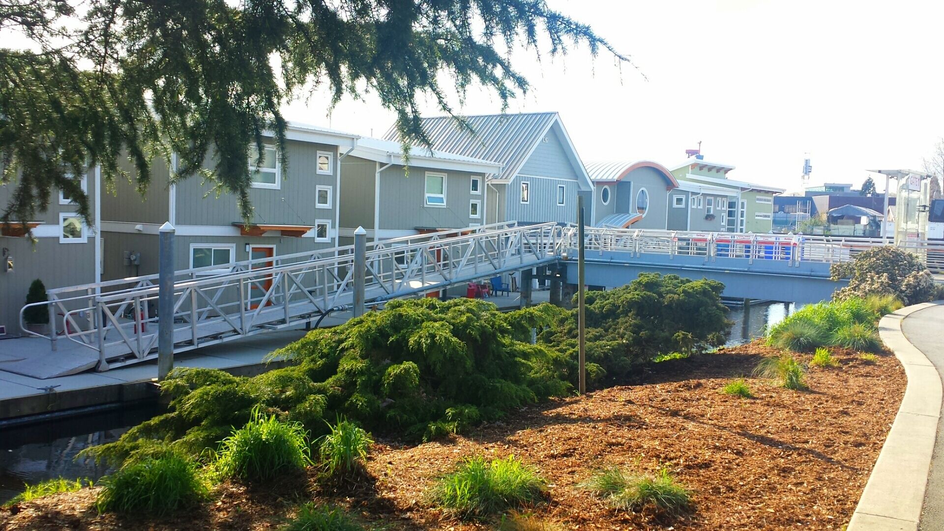 Een woongebied met een voetgangersbrug die twee gebouwen verbindt, omringd door groen en een waterpartij.