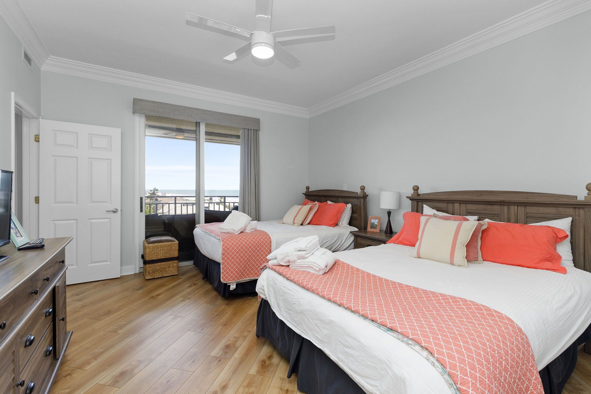 A hotel room with two beds, a ceiling fan, a view of the ocean, and a wooden dresser.