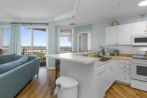 A modern kitchen with white cabinetry, a central island, and a view of the beach through large windows.