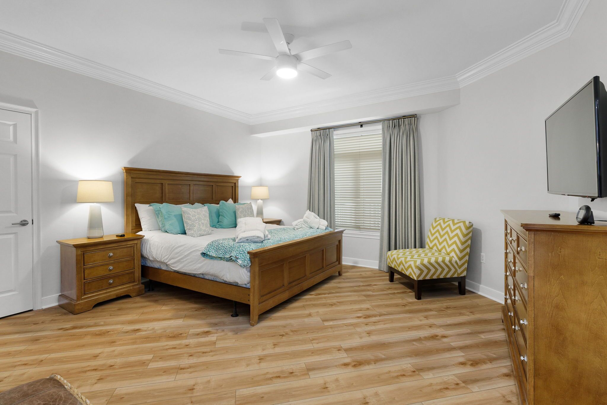 A bedroom with a wooden bed, nightstands, a chair, a dresser, and a ceiling fan.