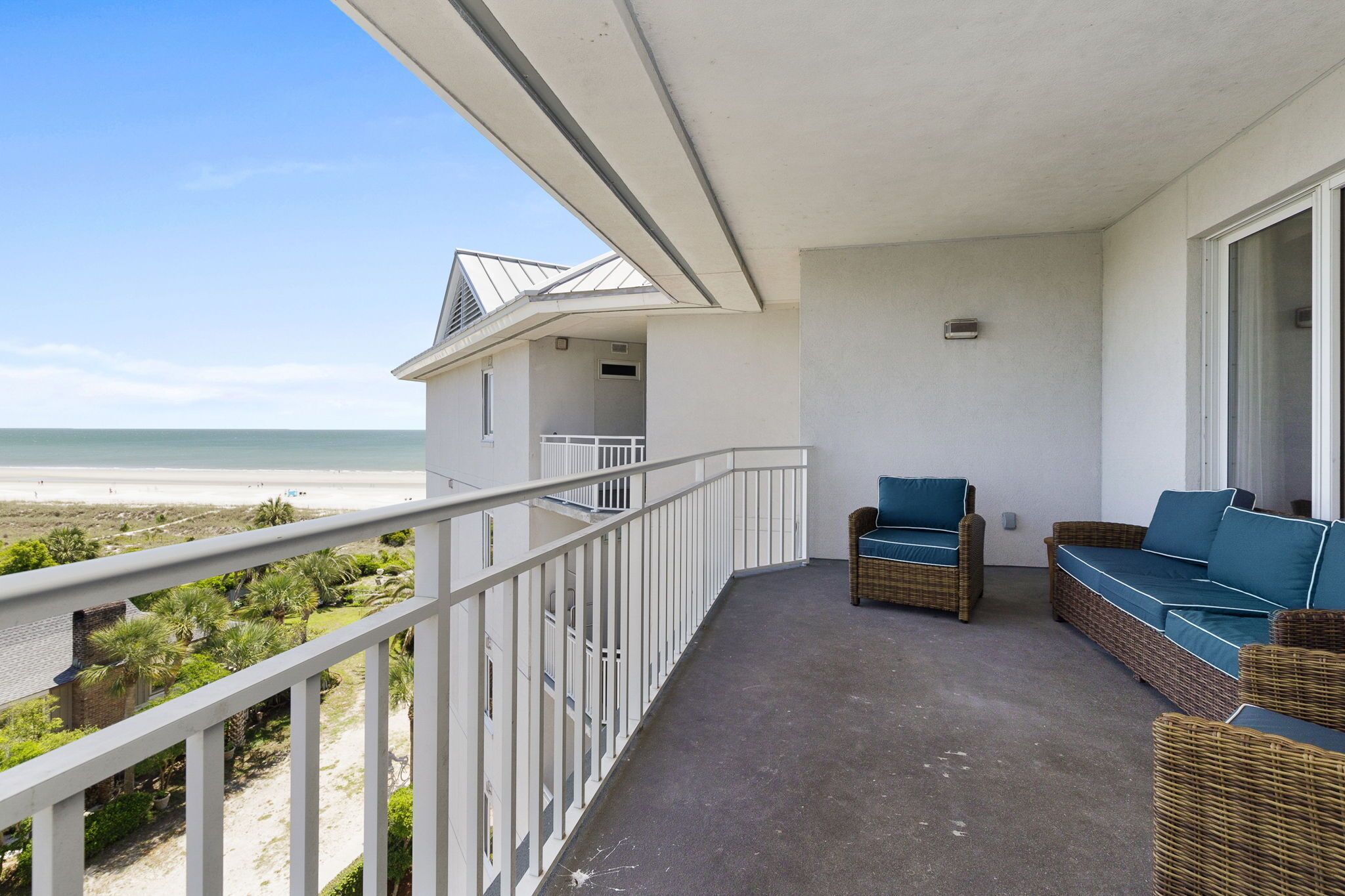 Un balcon donnant sur la plage, des meubles en osier et une balustrade blanche.