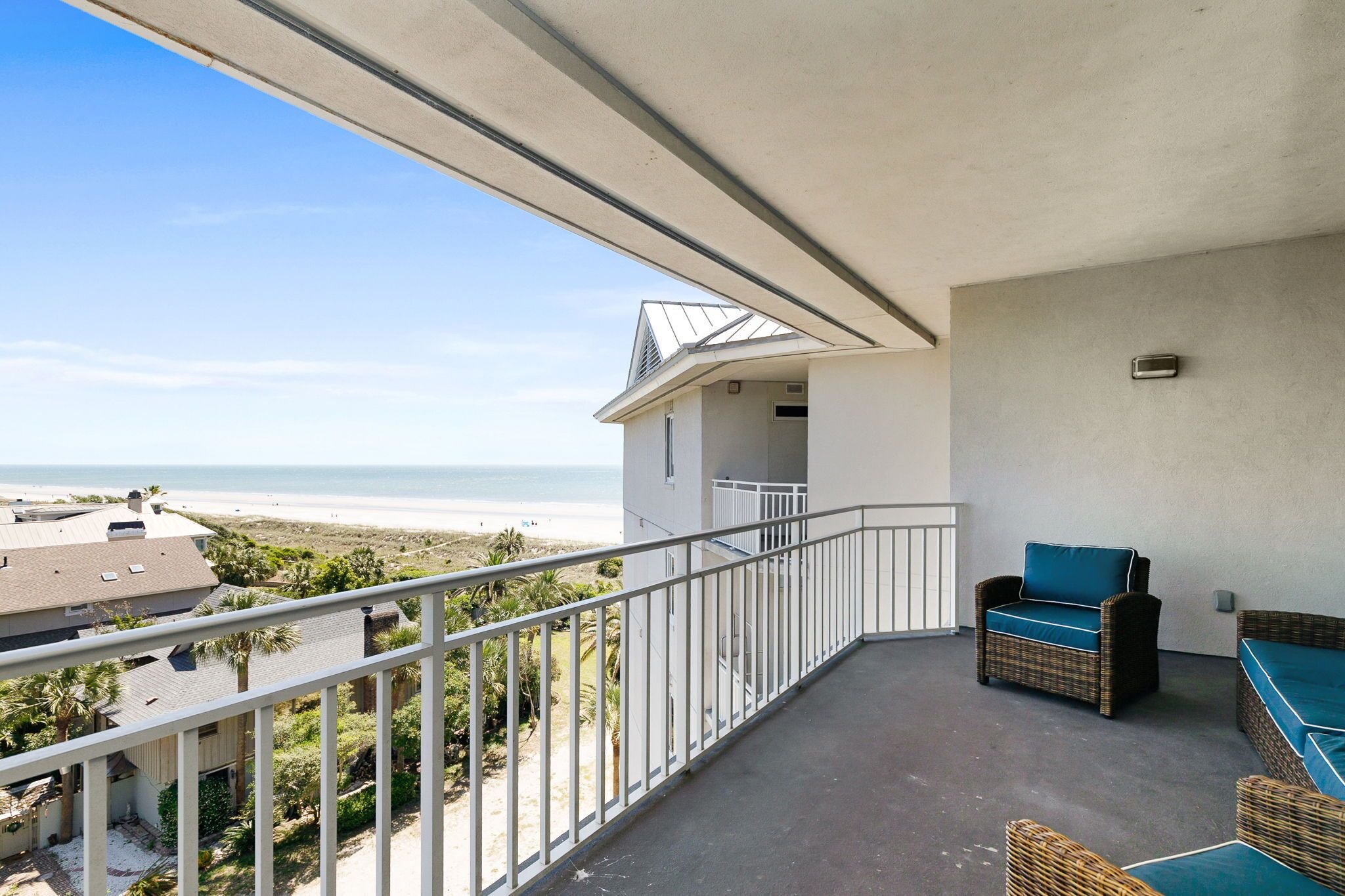 A balcony with a view of the beach, wicker furniture, and a concrete floor.