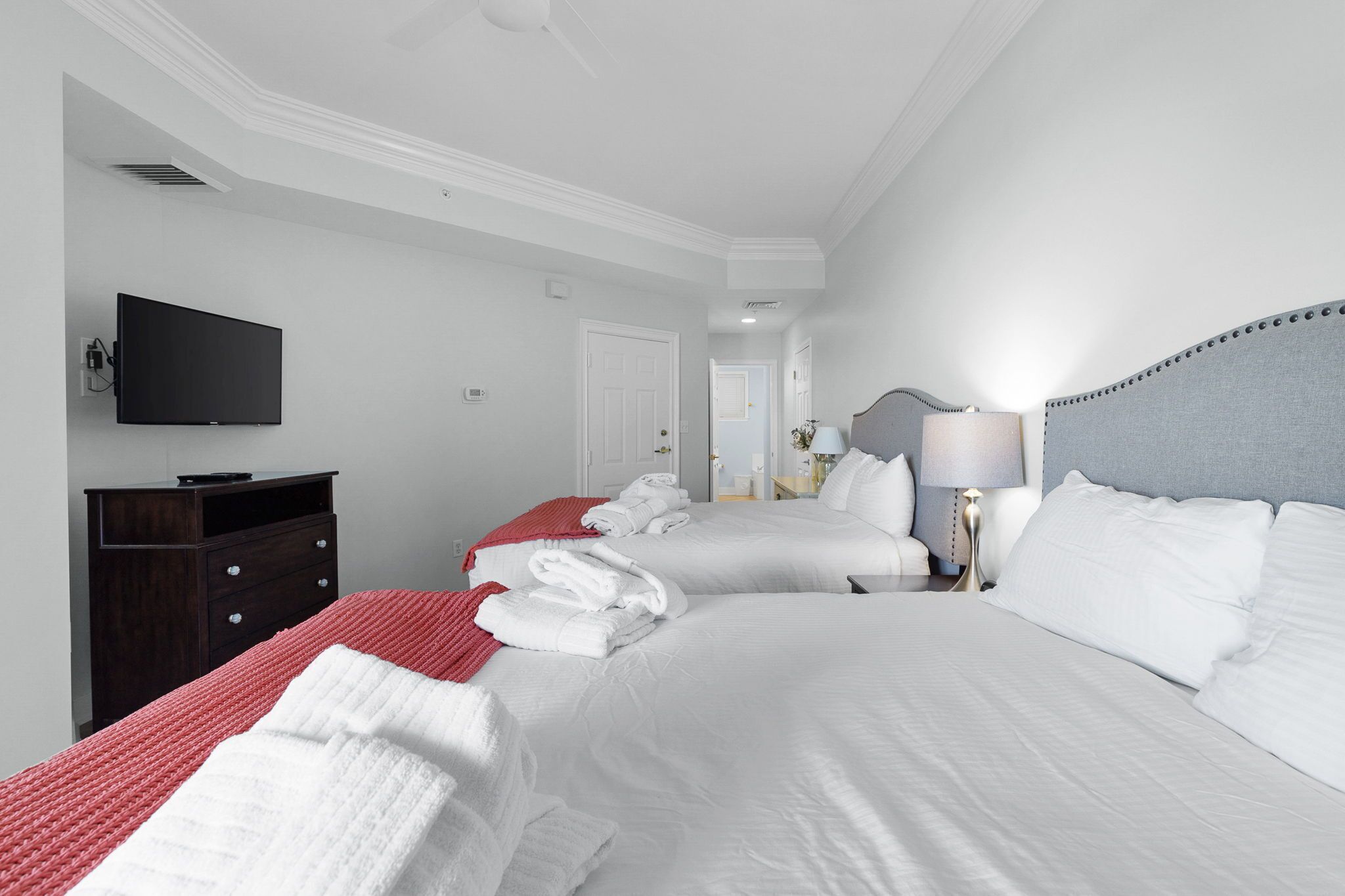 A hotel room with two beds, a flat-screen TV, a dresser, and a lamp.