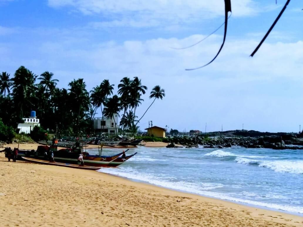 Ein Strand mit Booten, Palmen und einem Gebäude im Hintergrund.