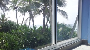 A window with a view of palm trees and a body of water. - Malika's Yellow House (Hikkaduwa)