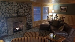 Un salon chaleureux avec une cheminée en pierre, un canapé en cuir et un pouf à rayures.