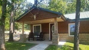 Un chalet doté d’un porche couvert, de piliers en pierre et de deux fauteuils Adirondack.