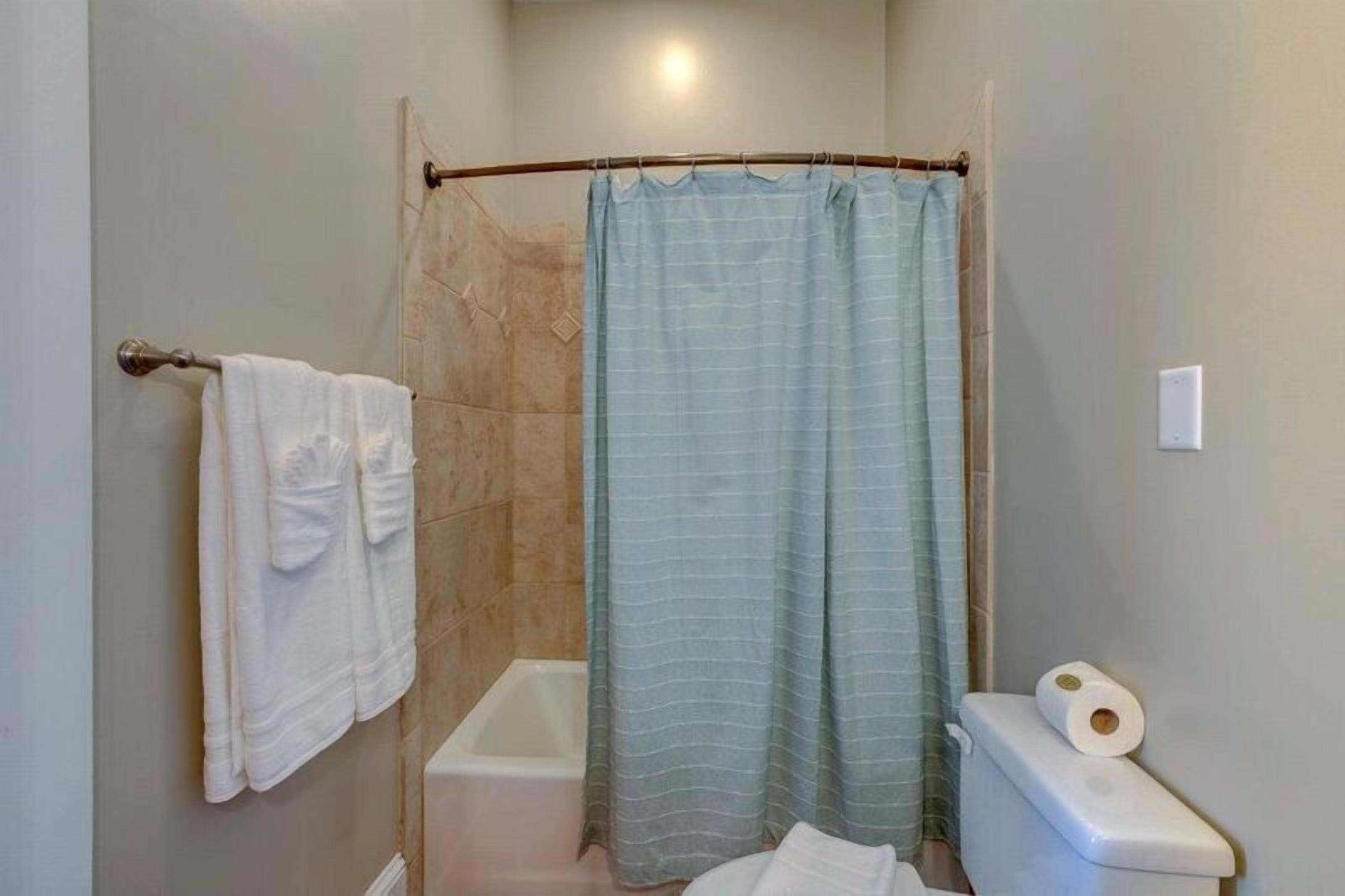 A bathroom with a shower curtain, a bathtub, and a toilet.
