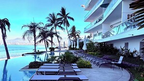 A poolside area with lounge chairs and palm trees, overlooking a body of water. - Beautifully decorated Beachfront/Oceanfront Luxury Condo in Bucerias  (Bucerias)