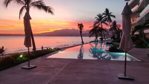 A poolside view with palm trees, a sunset, and a distant mountain range.