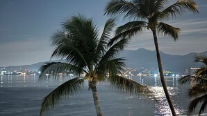 A beach with palm trees, a wooden sign, and a cityscape in the background. - Beautifully decorated Beachfront/Oceanfront Luxury Condo in Bucerias  (Bucerias)