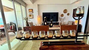 A modern living room with a glass coffee table holding several glass candle holders, a flat-screen TV, and decorative wall art. - Beautifully decorated Beachfront/Oceanfront Luxury Condo in Bucerias  (Bucerias)