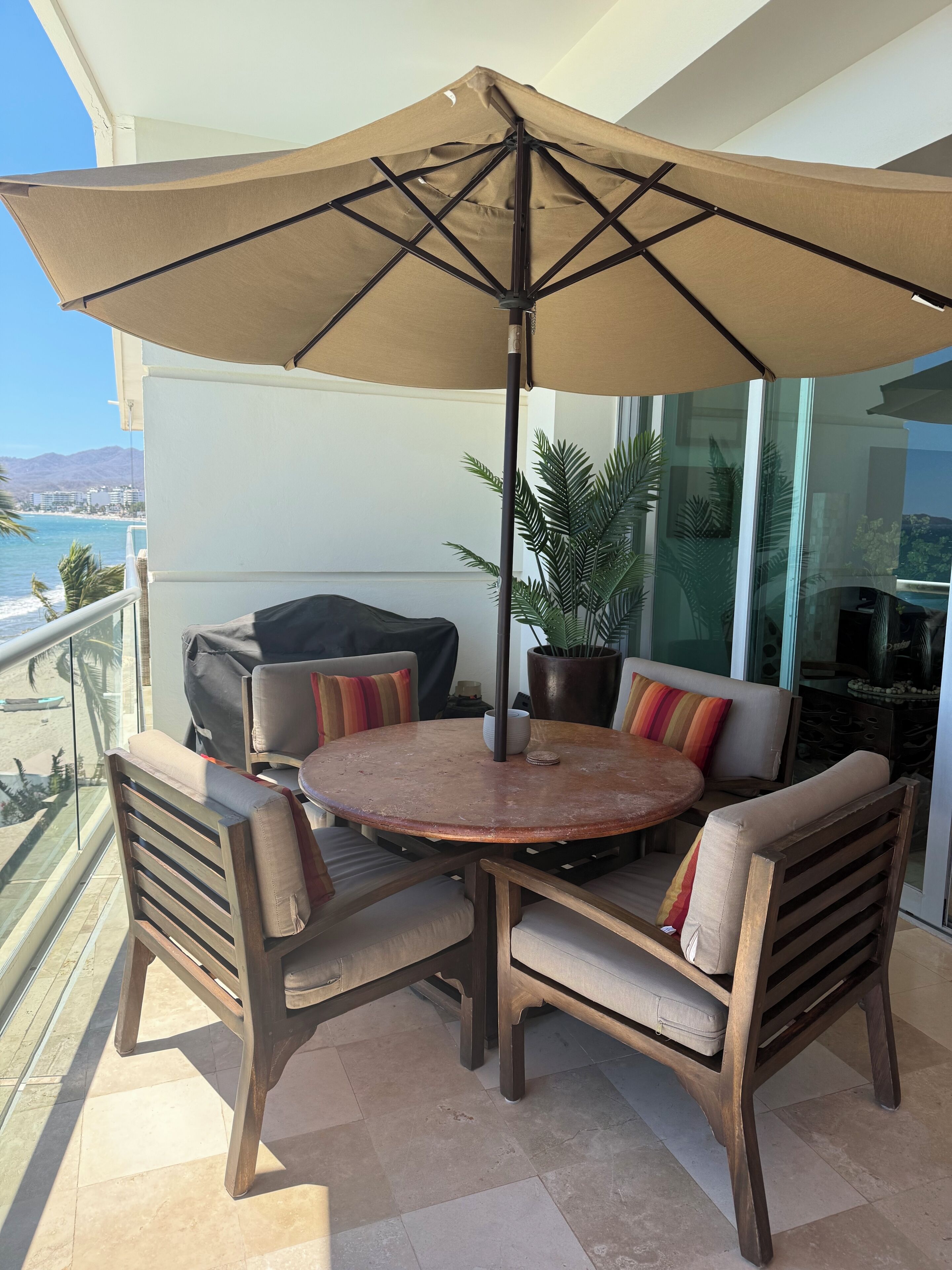 A balcony with a round table, chairs, a large umbrella, and a view of the ocean.