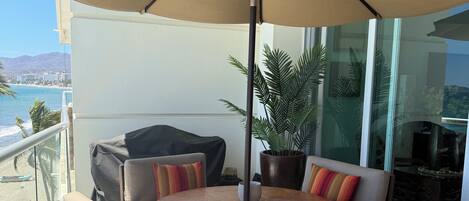 A balcony with a round table, chairs, a large umbrella, and a view of the ocean.