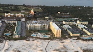 Vue aérienne d’une station balnéaire comprenant plusieurs bâtiments d’hôtel, une plage de sable et une vaste étendue d’eau en arrière-plan.