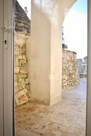 Step into a serene outdoor space with a stone wall and a white column, surrounded by a light-colored tile floor.
