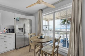 Enjoy a functional kitchen with a refrigerator, water dispenser, and dining area with a round table and two chairs, offering a view of the beach and ocean.