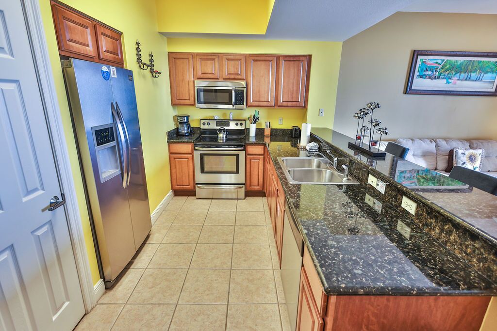 A kitchen with wooden cabinets, a stainless steel refrigerator, a microwave, a stove, and a granite countertop.