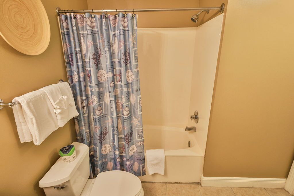 A bathroom with a toilet, a bathtub, and a shower curtain with a nautical theme.