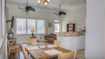 A dining area with a wooden table, chairs, and a chandelier. There is a kitchen area with a countertop and cabinets.