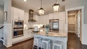 A modern kitchen with white cabinetry, stainless steel appliances, a marble island with bar stools, and pendant lighting.
