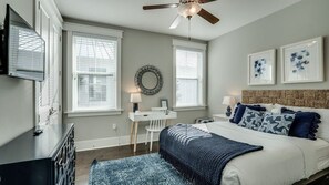 A bedroom with a bed, bedside tables, a desk, and a ceiling fan.