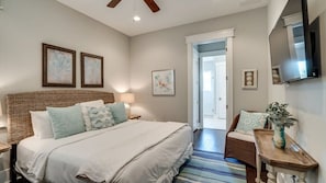 Une chambre avec un grand lit, une tête de lit en osier, une table de chevet avec une lampe et un téléviseur fixé au mur.