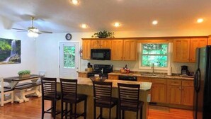 Una cocina con armarios de madera, un microondas y un refrigerador. Hay un comedor con una mesa y sillas.
