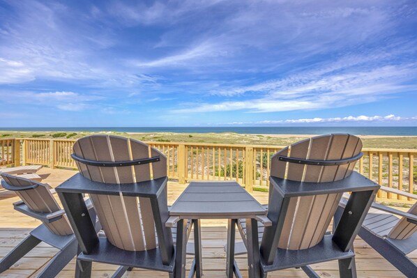 A deck with two Adirondack chairs and a small table, overlooking a beach with a wooden railing. - Oceanfront Home in Avon with Hot Tub, Game Room, and Direct Beach Access (Avon)