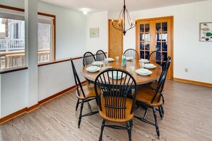A dining area with a round table, six chairs, and a chandelier. - Oceanfront Home in Avon with Hot Tub, Game Room, and Direct Beach Access (Avon)