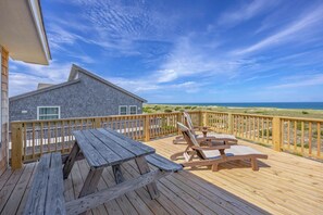 A wooden deck with a picnic table and lounge chairs overlooking a beach. - Oceanfront Home in Avon with Hot Tub, Game Room, and Direct Beach Access (Avon)