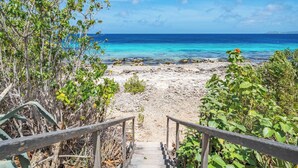 Una escalera de madera que conduce a una playa con aguas turquesas cristalinas y un cielo despejado.