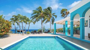 Una piscina con sillones de descanso, palmeras y vistas al océano.