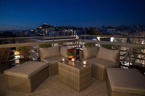 A rooftop terrace with wicker furniture, a small table with candles, and a view of a cityscape at dusk. - Make some family memories - 4 bd/4ba, views, W/D, WiFi (Athens)