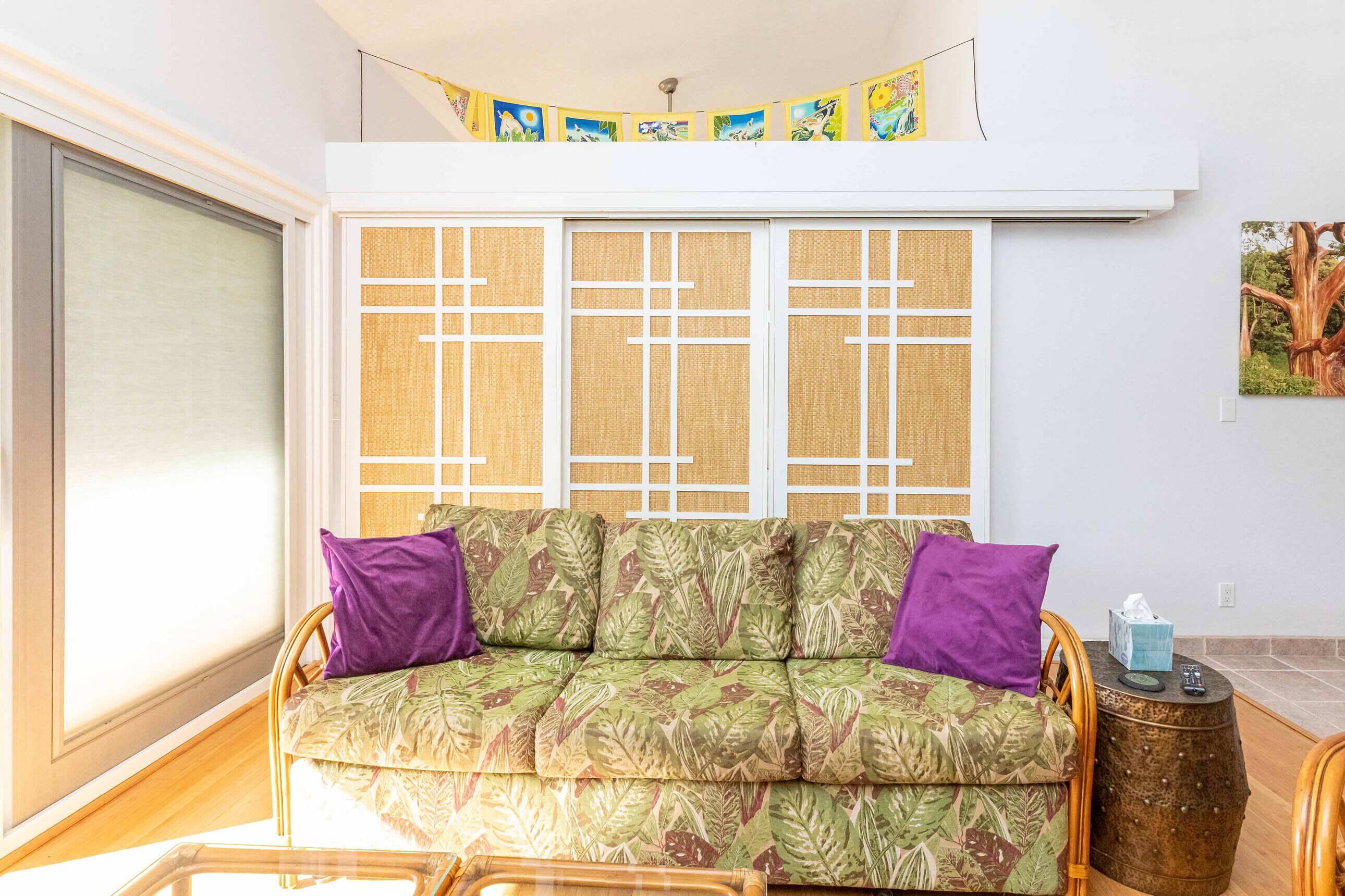 A room with a sofa, a small wooden side table, and a large window with a view.