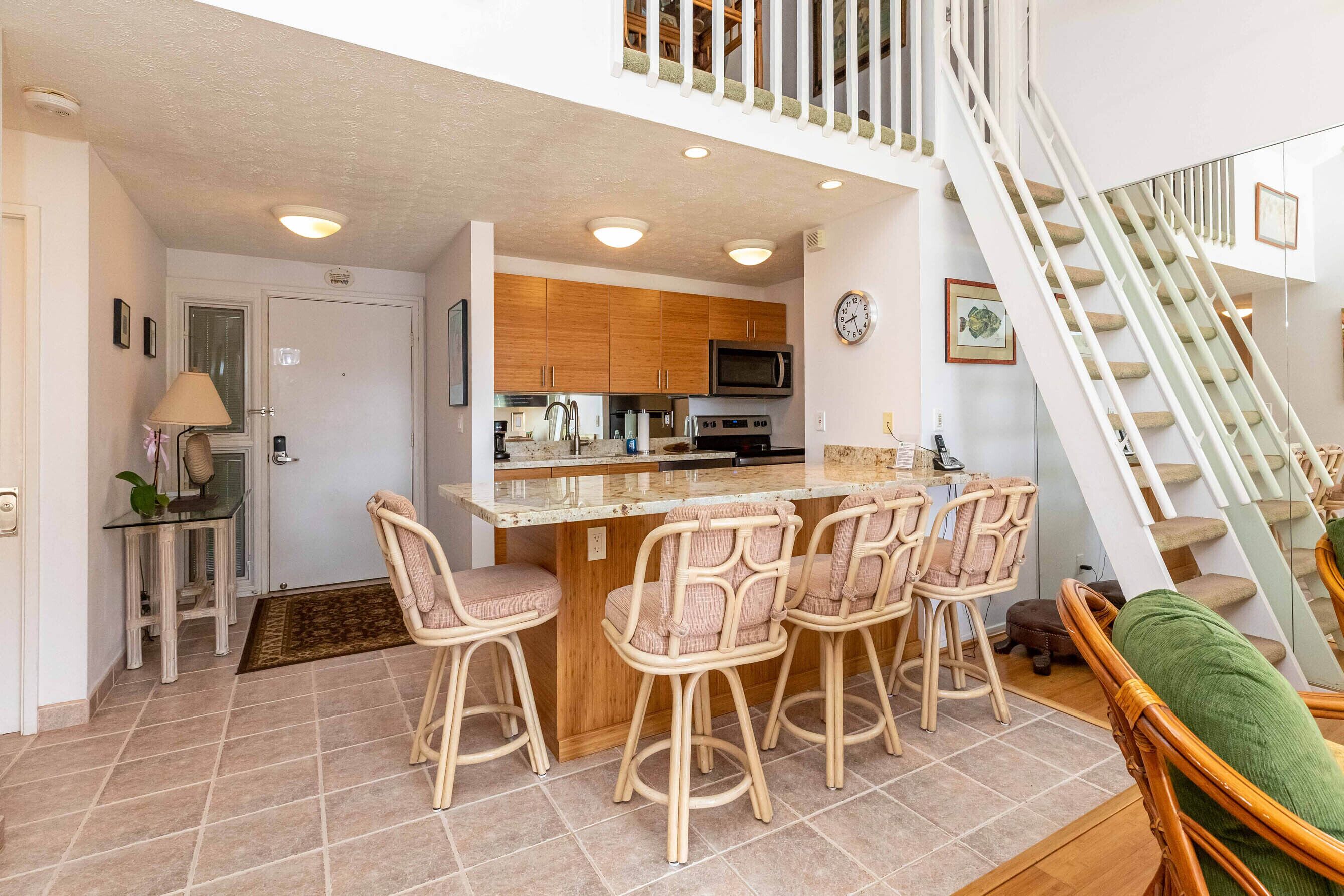 A kitchen with a central island, wooden cabinets, and a microwave. There are four wicker chairs around the island.