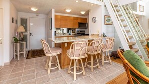 A kitchen with a central island, wooden cabinets, and a microwave. There are four wicker chairs around the island.