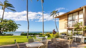 A beachfront patio with outdoor seating, a grill, and a view of the ocean.