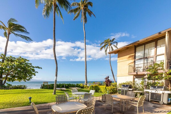 A beachfront patio with outdoor seating, a grill, and a view of the ocean.