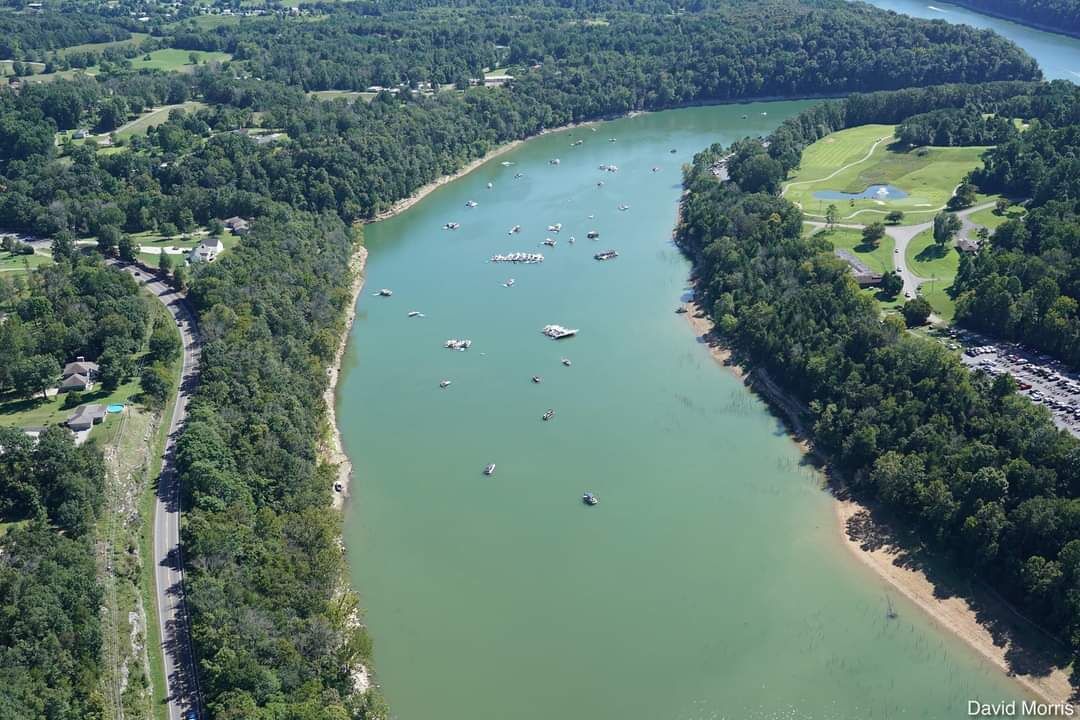 An aerial view of a river with boats, surrounded by dense greenery and a golf course.