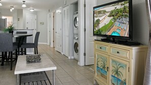 A hotel room with a dining area, a washing machine, and a television displaying a beach scene. - Surf Beach 502 - Spectacular Sunsets - Beach Front (Treasure Island)