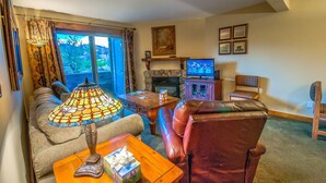 A cozy living room with a sofa, a leather chair, a table with a lamp, a fireplace, and a television. - Cozy condo in Steamboat Springs.  Close to slopes! (Steamboat Springs)